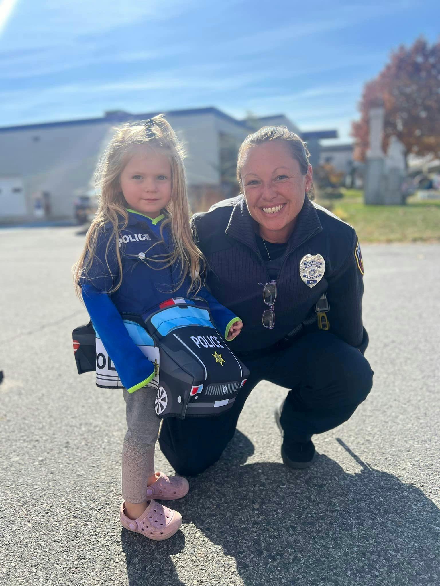 Child in police costume with toy police car next to person in police uniform