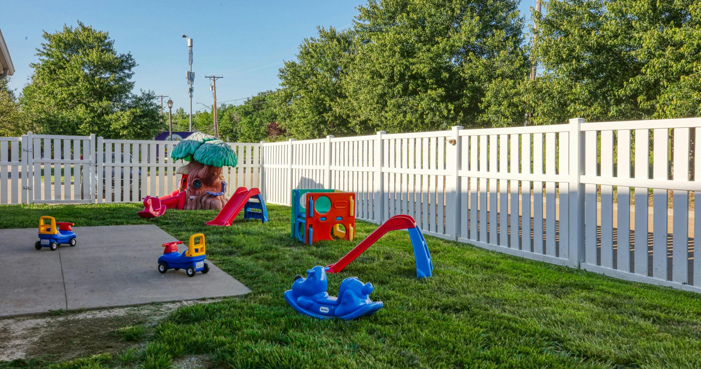 Children's playground with small slides and ride-on toys inside a fenced area