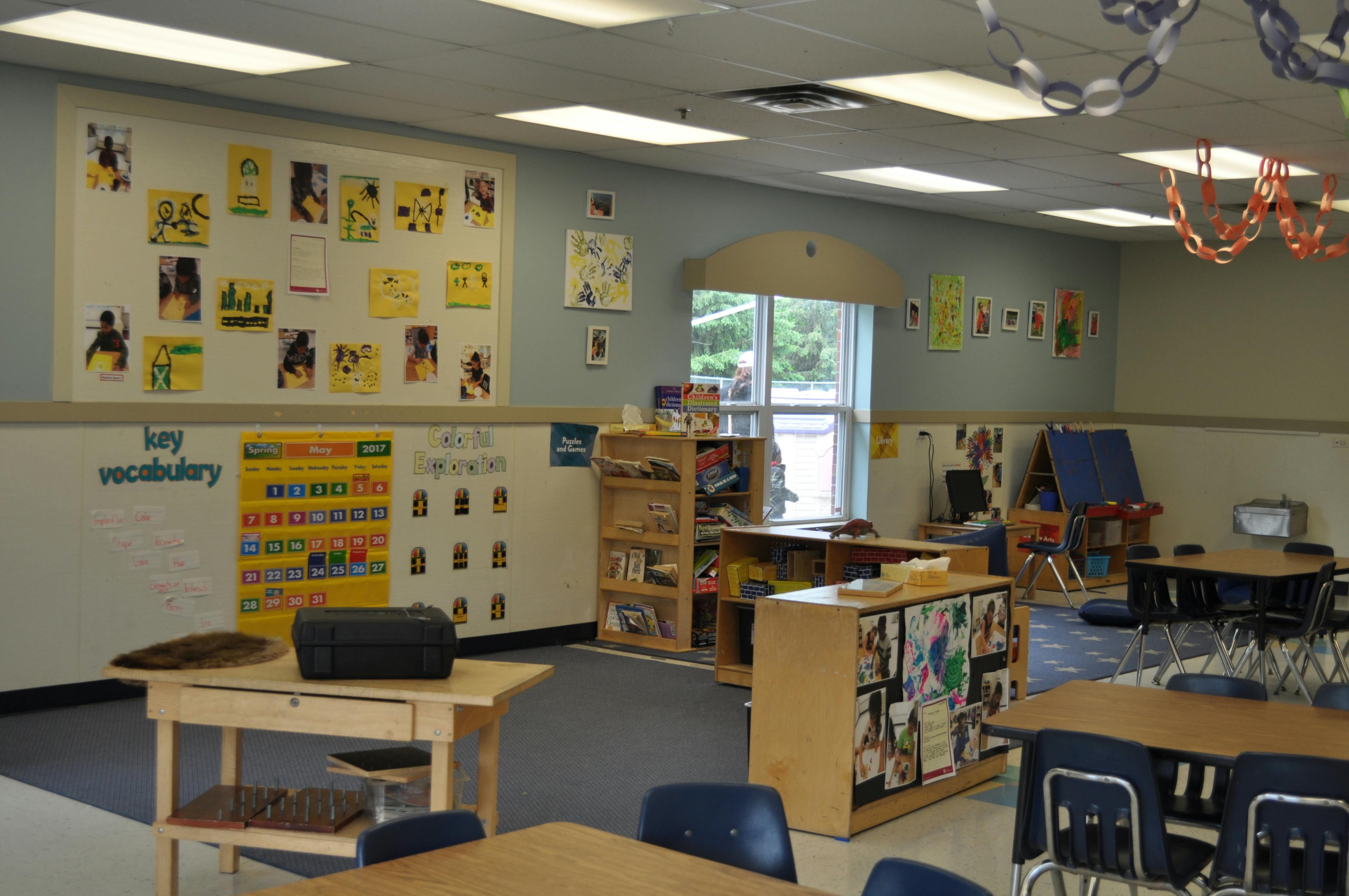 An empty classroom with desks, chairs, and shelves decorated with student artwork