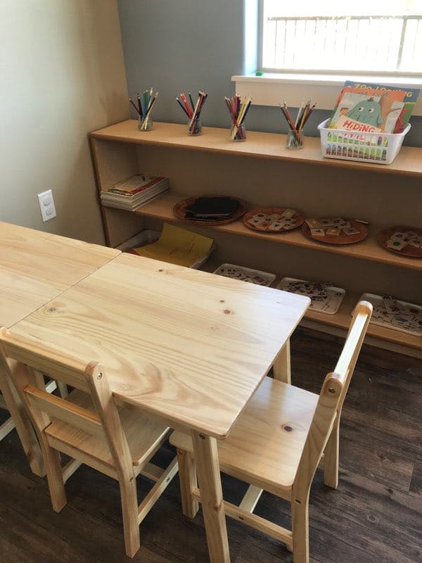 Small wooden tables and chairs in a classroom with shelves of supplies
