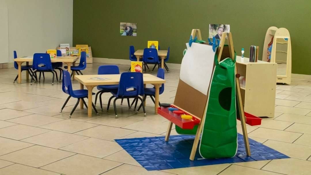 Classroom with small tables and chairs, and an easel