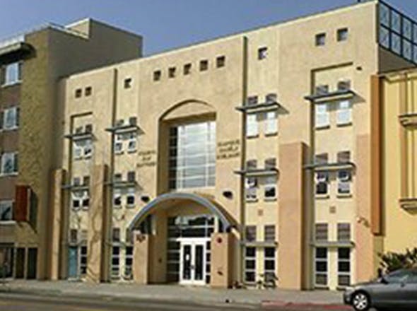 Tan building with an arched entrance, many windows, and some overhangs