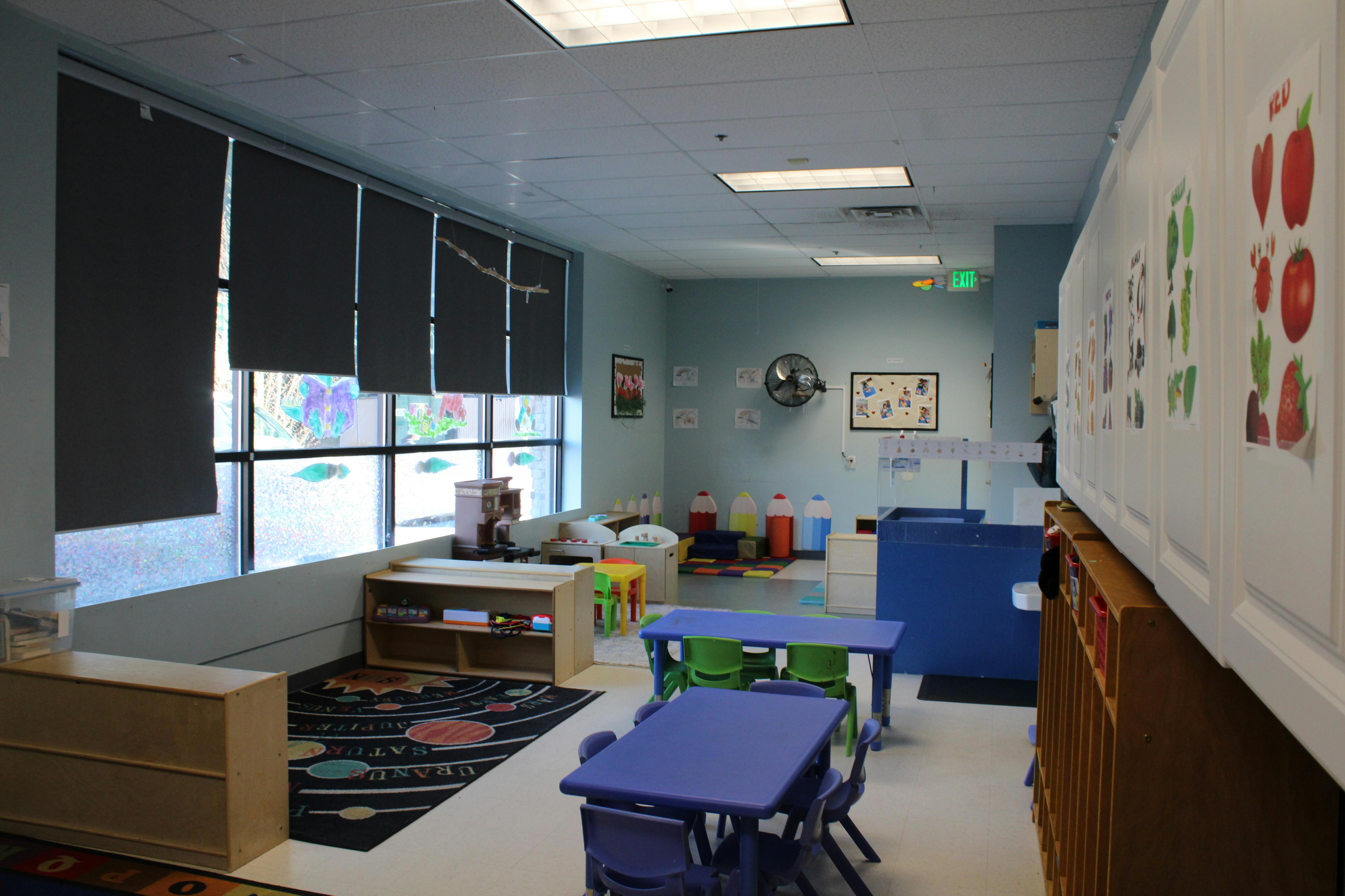 Classroom with child-sized tables and chairs, window with blinds, and cubbies