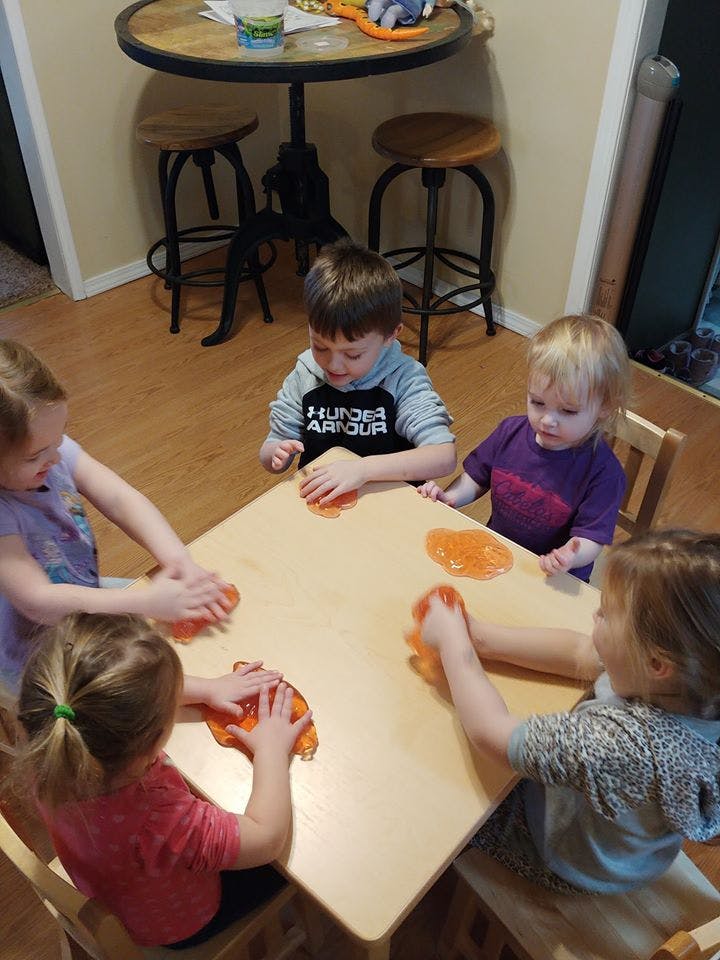 Four children playing with orange slime at a small table