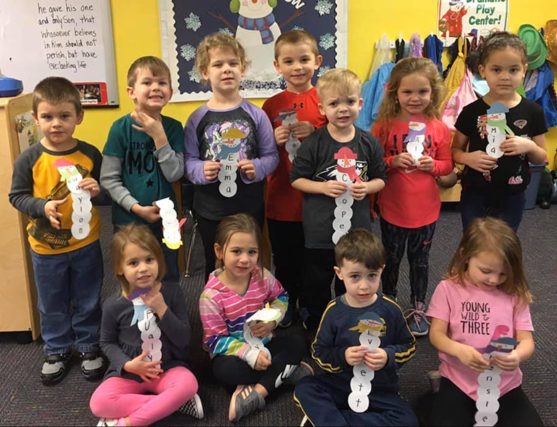 Group of children holding paper snowman crafts in a classroom