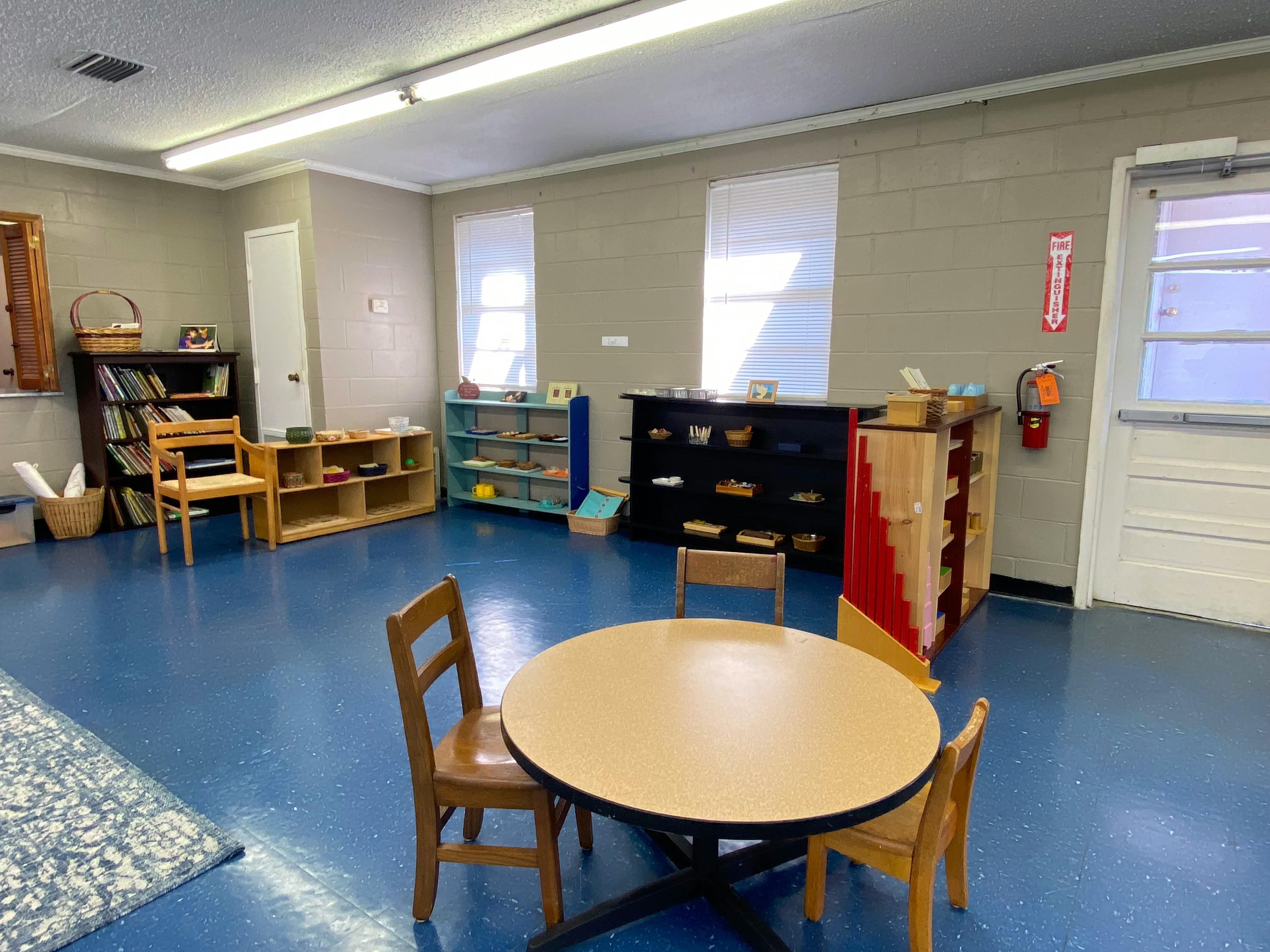 Classroom with small tables and chairs, shelves with learning materials
