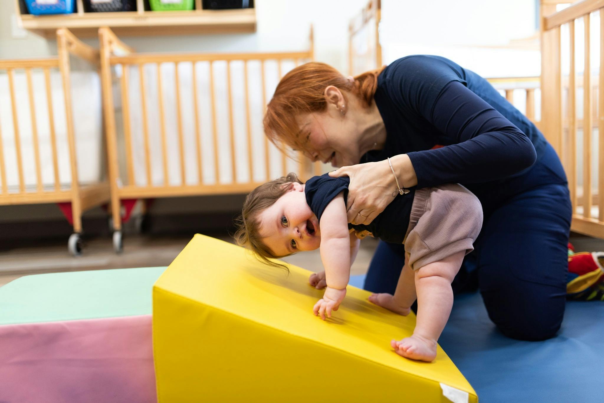 Adult helping a child climb on a soft yellow ramp in a play area