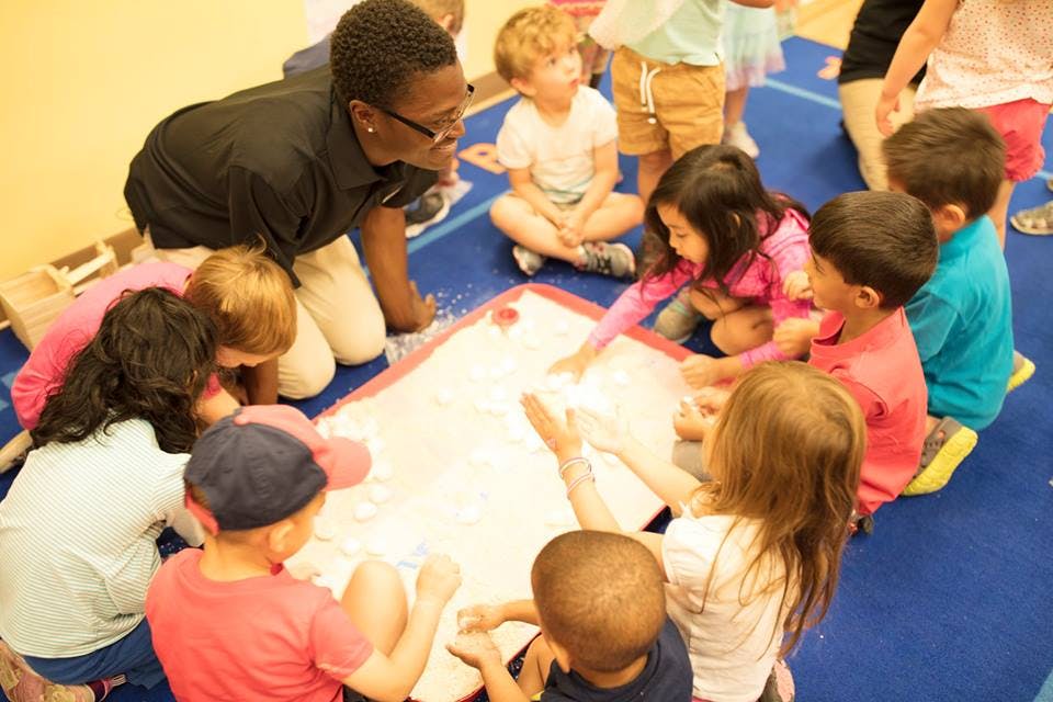 Adult and children gathered around a white mat on the floor