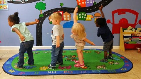 Four children playing on a rug in a room with a painted mural
