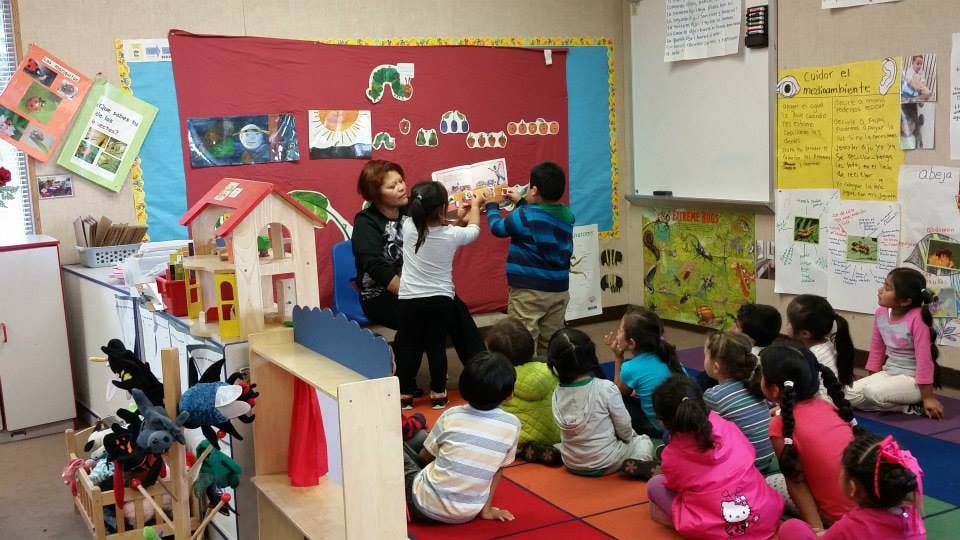 Adult and children reading a book to other children in a classroom