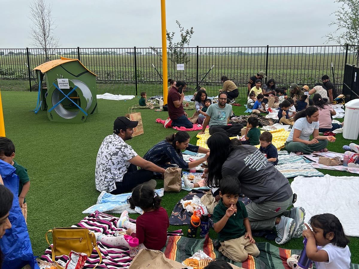 Many people and children sitting on blankets on a grassy area