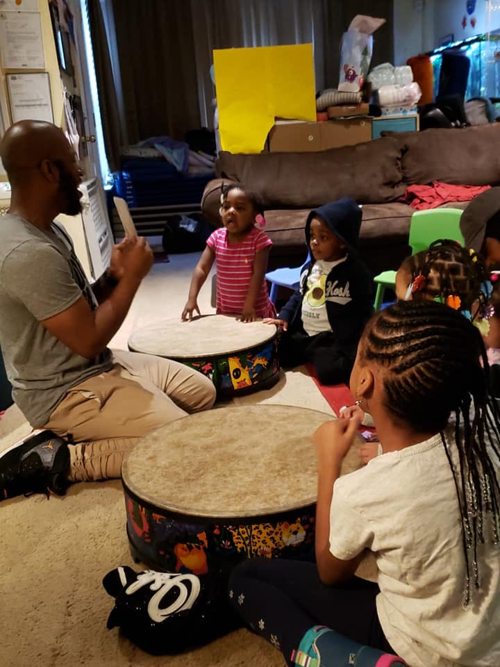 Person and children sitting on floor with drums