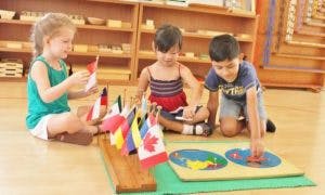 Three children playing with flags and a puzzle on the floor