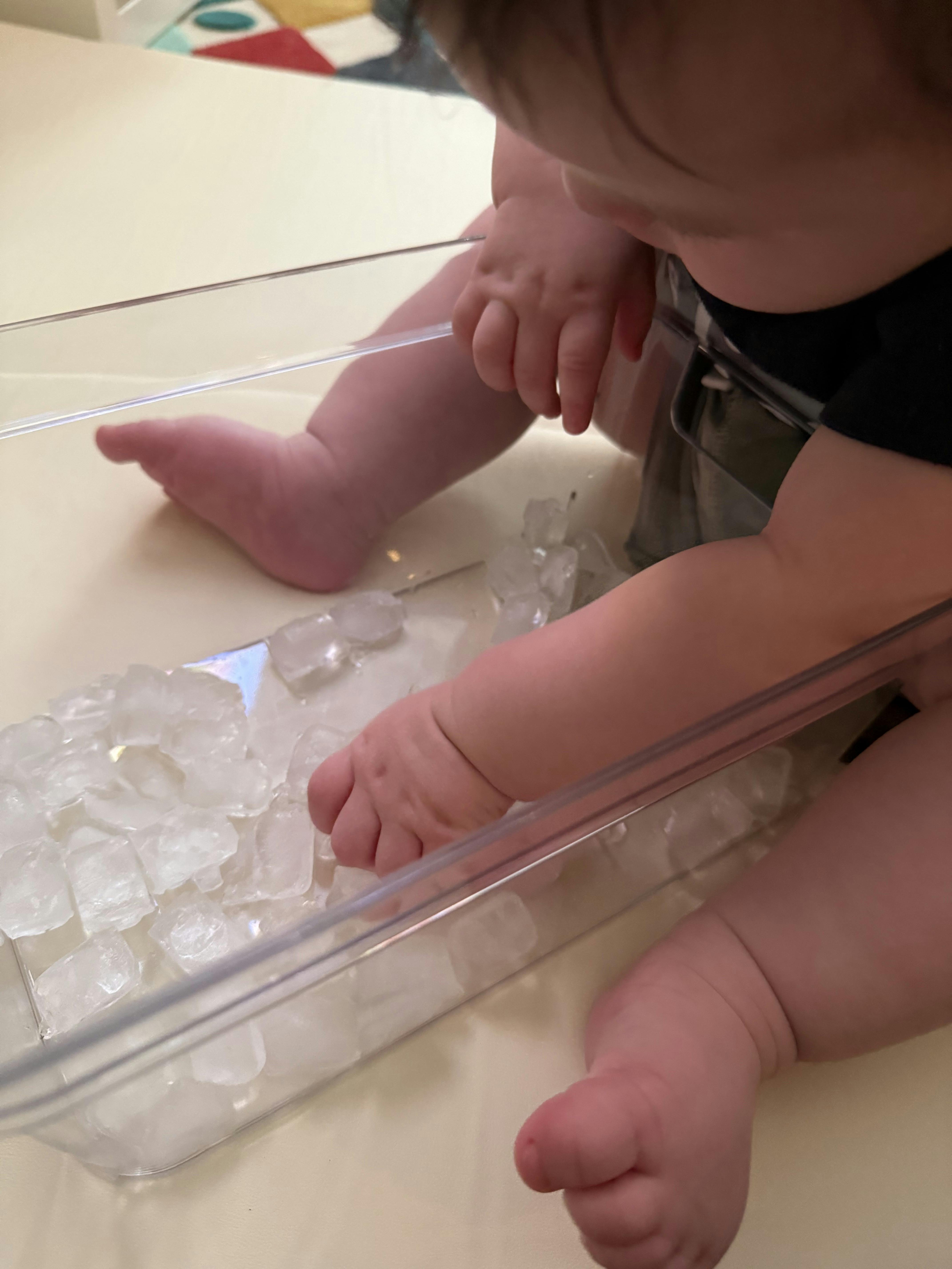 Child playing with ice cubes in a plastic container