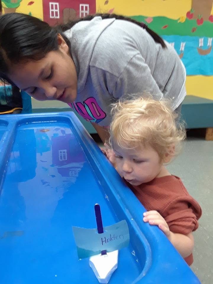 Person and child looking at a toy boat in a water table