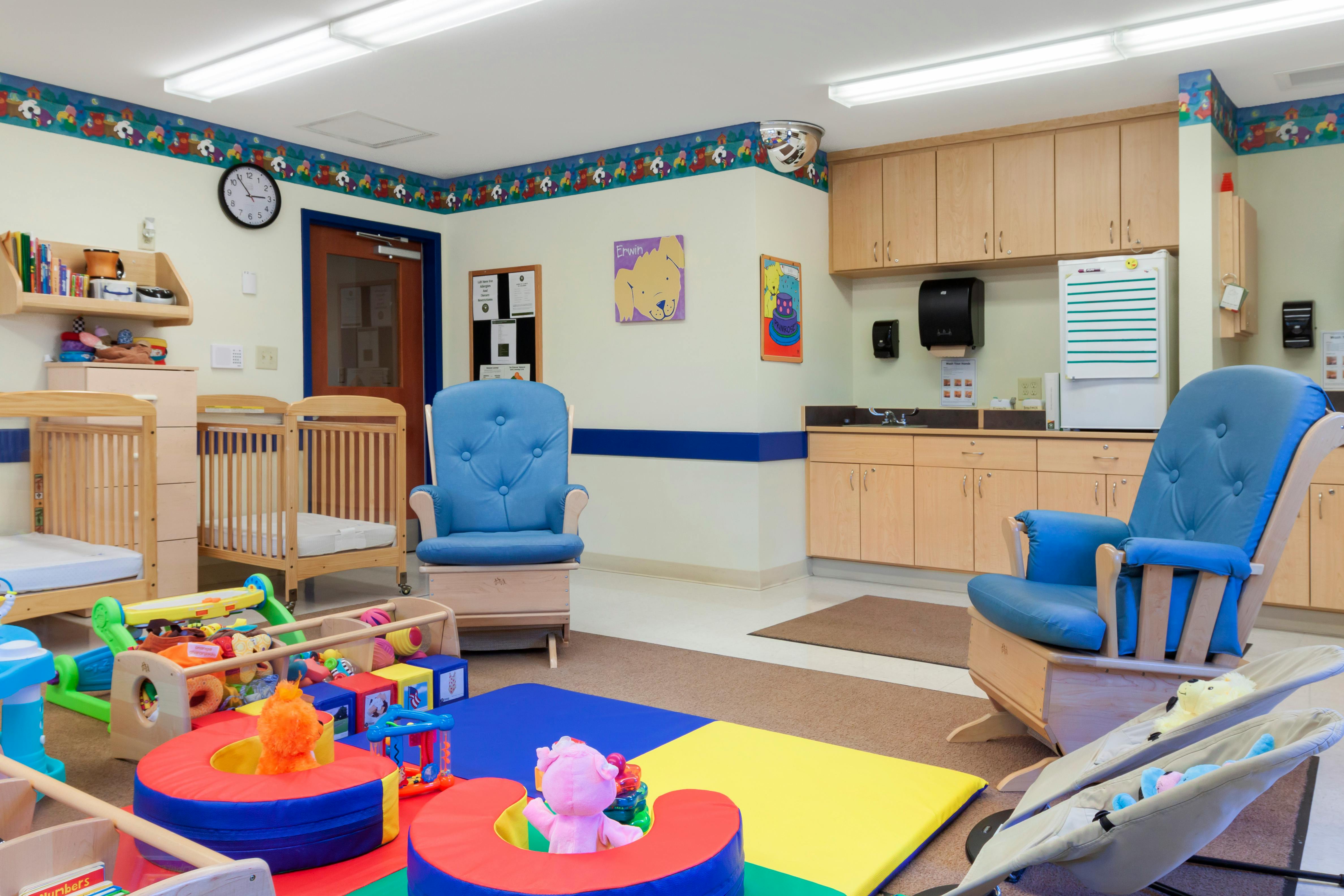 A playroom with two cribs, two rocking chairs, and colorful play mats on the floor