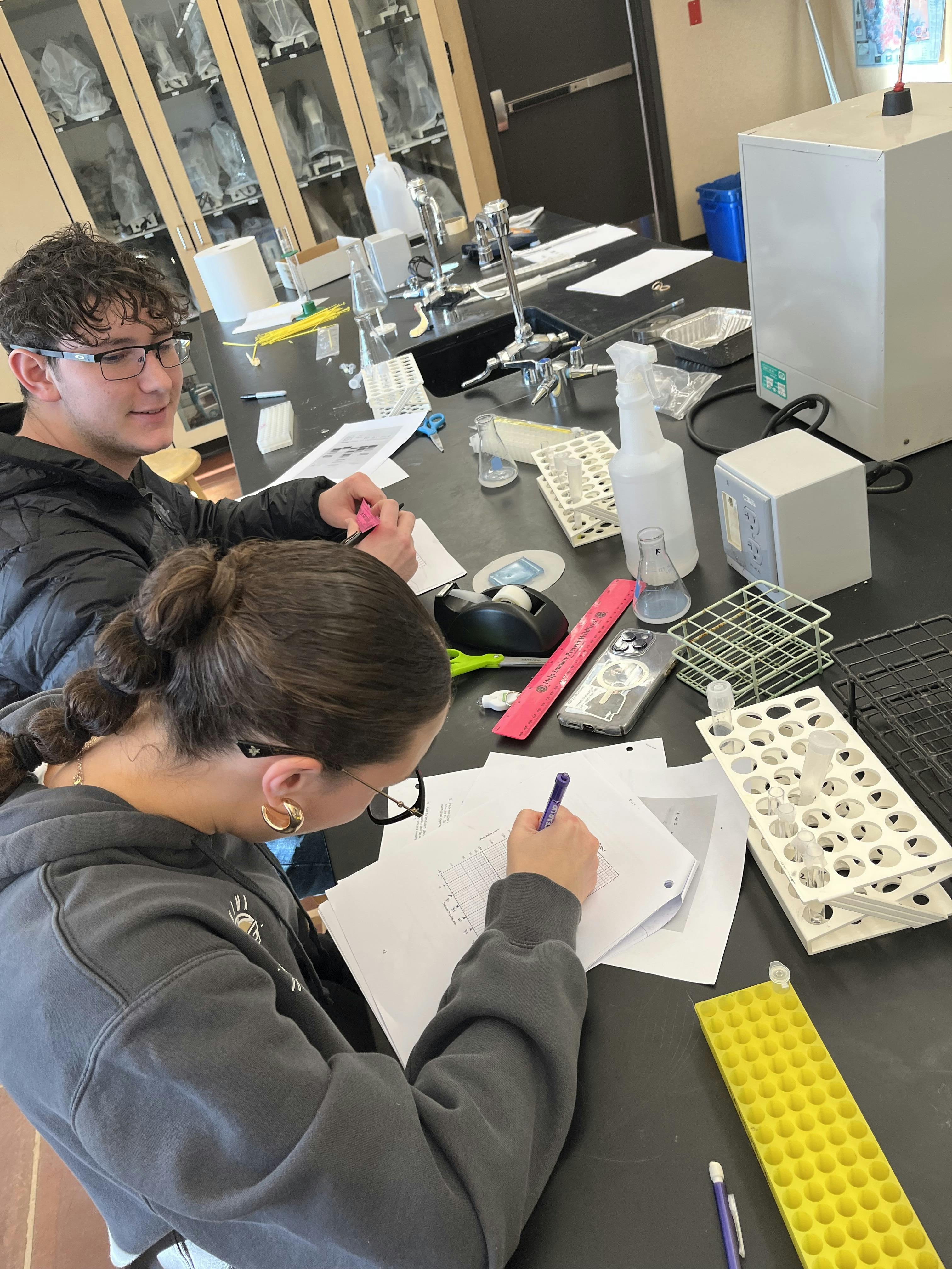 Two teens working at a lab table with scientific equipment