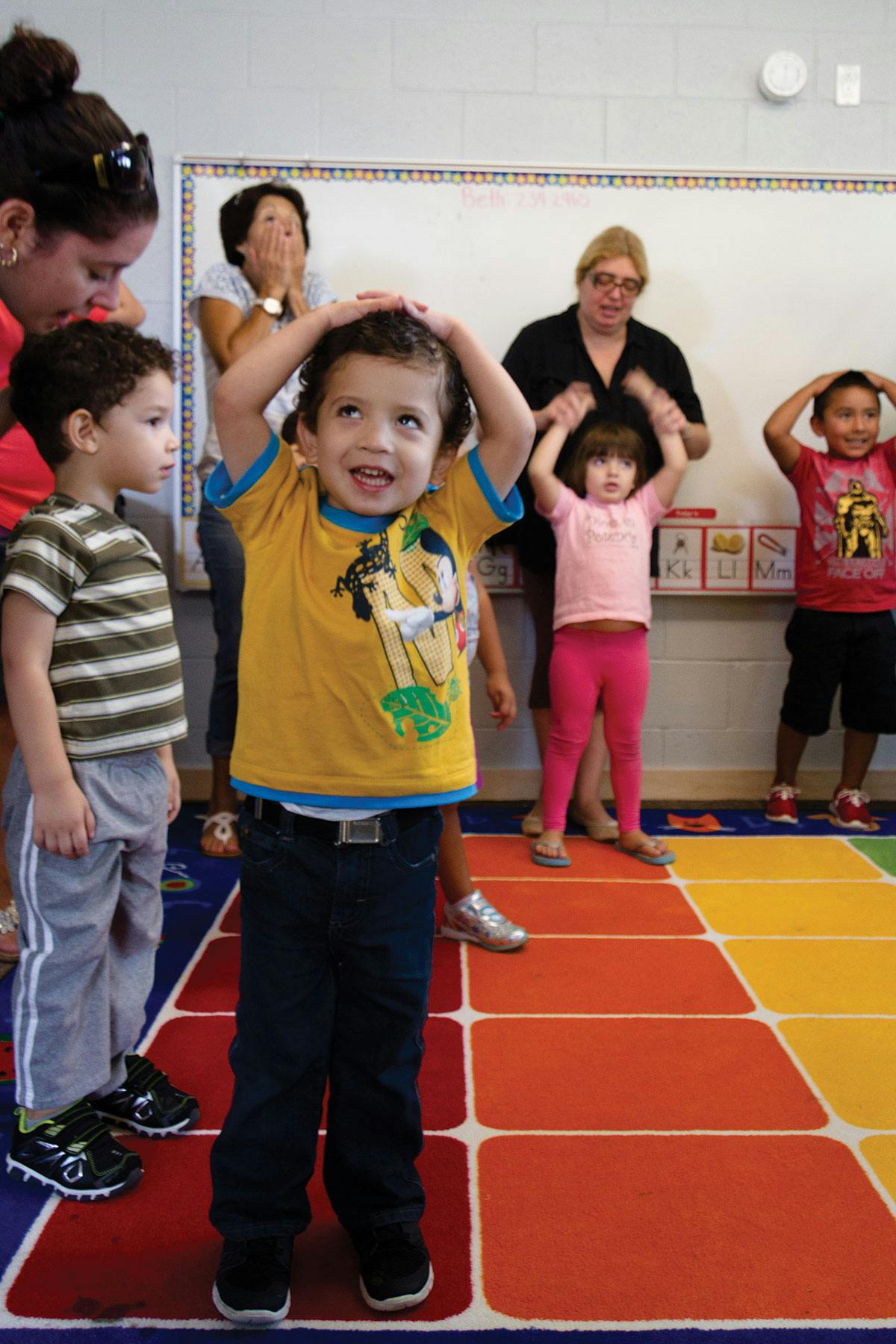 Children and adults in a classroom, children with hands on heads