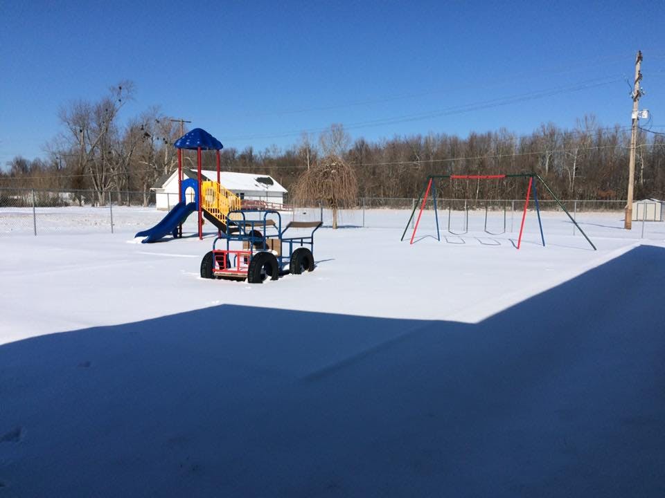 Playground with snow-covered ground, slide, swings, and small vehicle