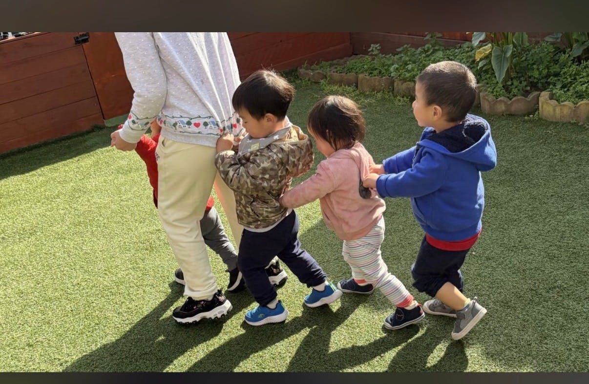 Three children holding onto the clothes of the person in front of them in a line