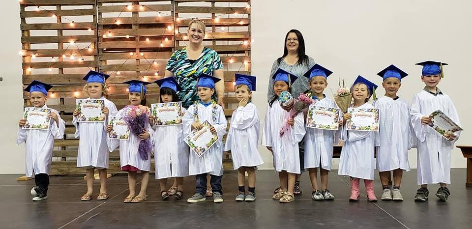Two adults with a group of children in graduation caps and gowns holding certificates
