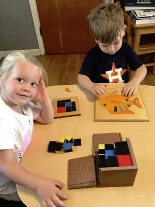 Two children playing with puzzles and blocks at a table