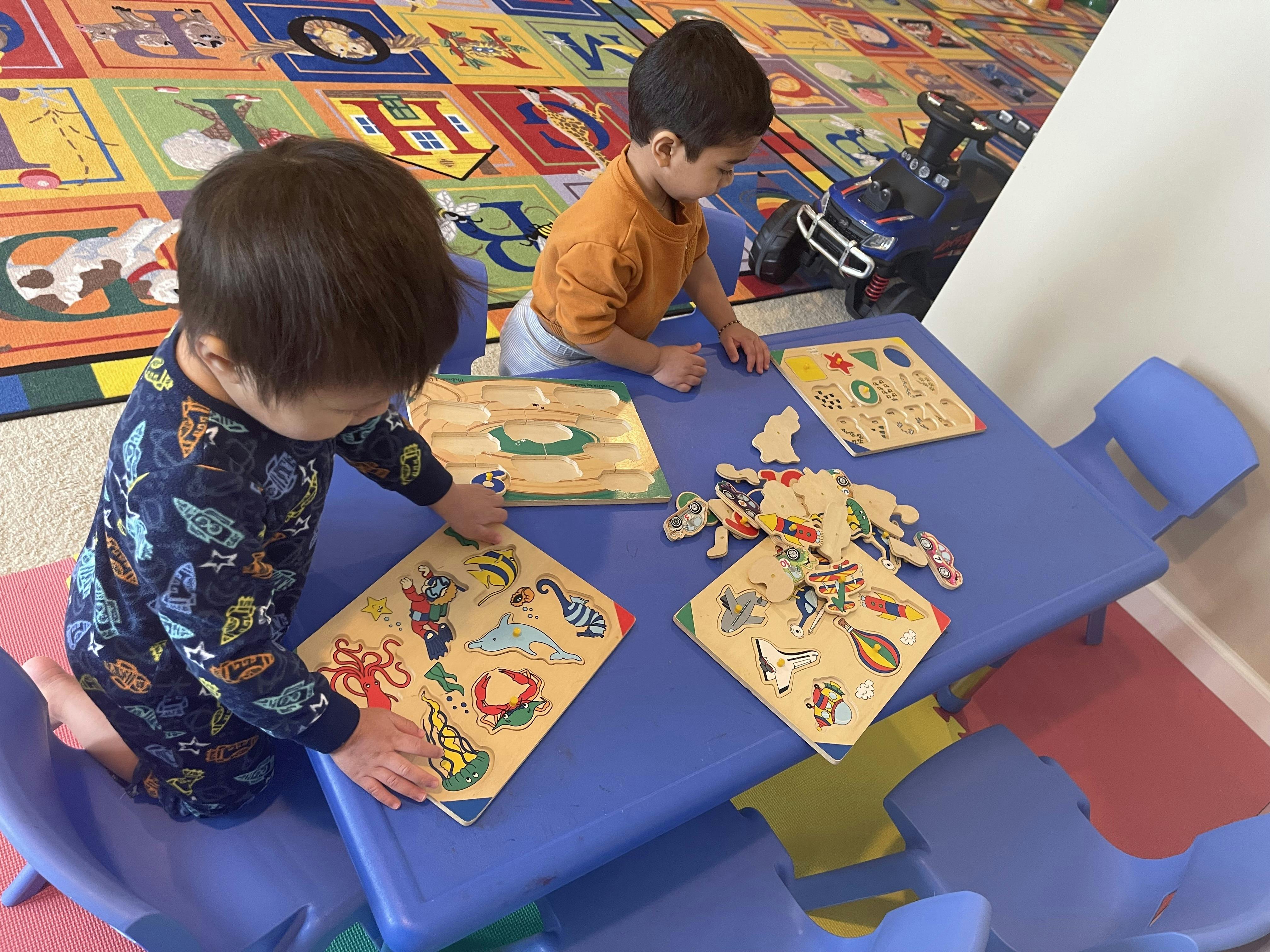 Two children playing with puzzles at a blue table