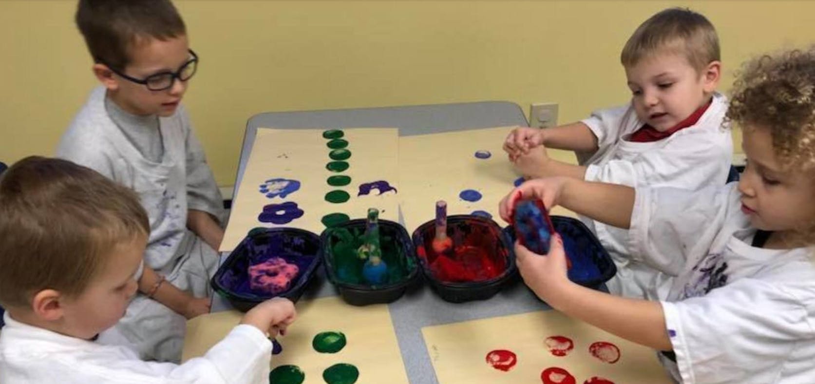 Four children painting with sponges at a table