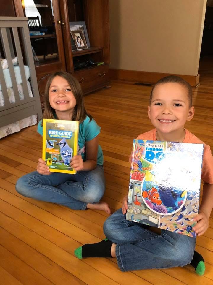 Two children sitting on a wooden floor holding books