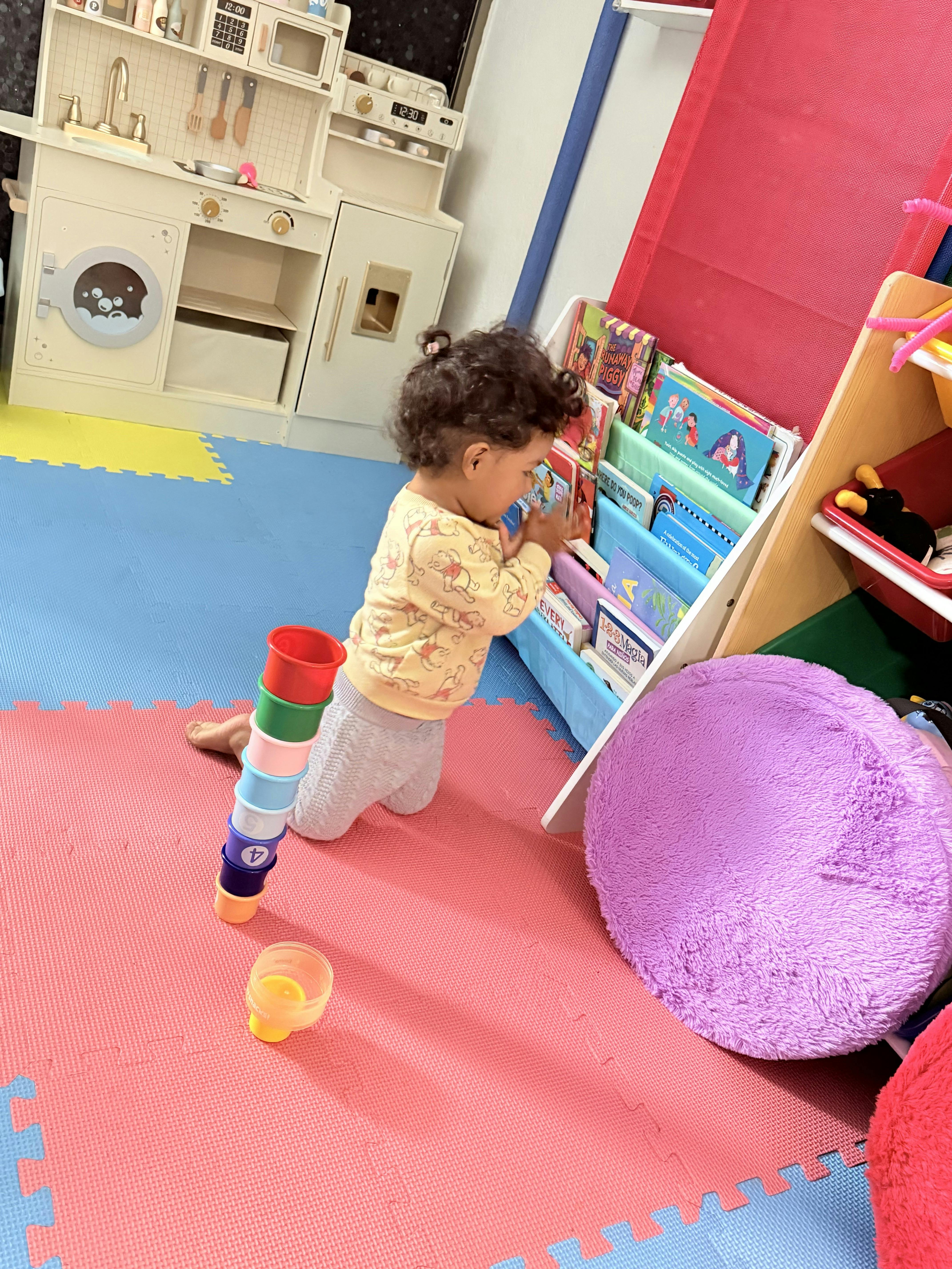 Child on hands and knees looking at books in a small shelf