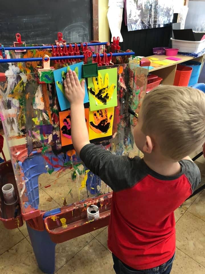 Child placing a handprint painting on an easel