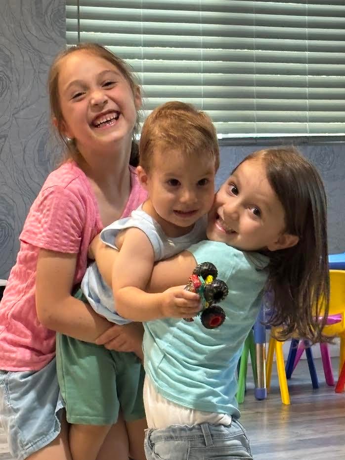 Three children hugging, the youngest child holding a toy truck