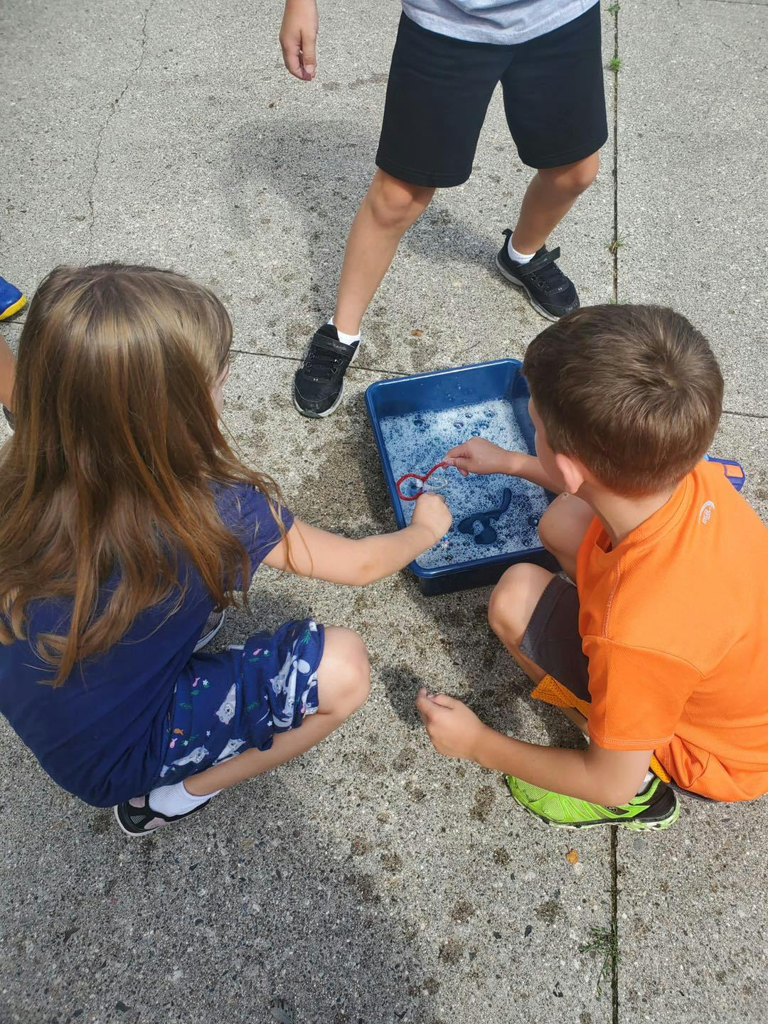 Two children playing with bubbles in a blue bin, rectangular container