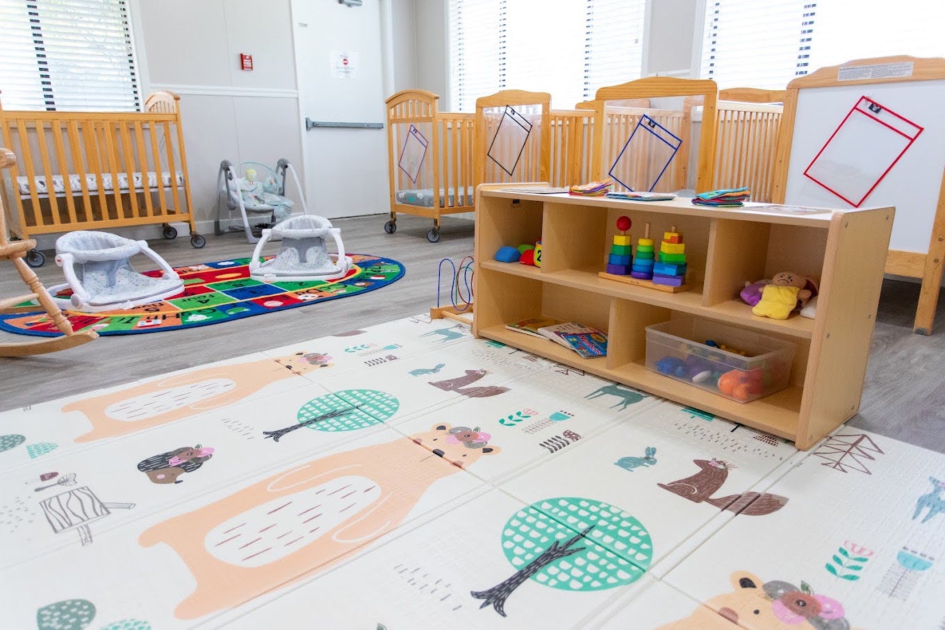 Cribs and toys in a daycare room with a colorful play mat