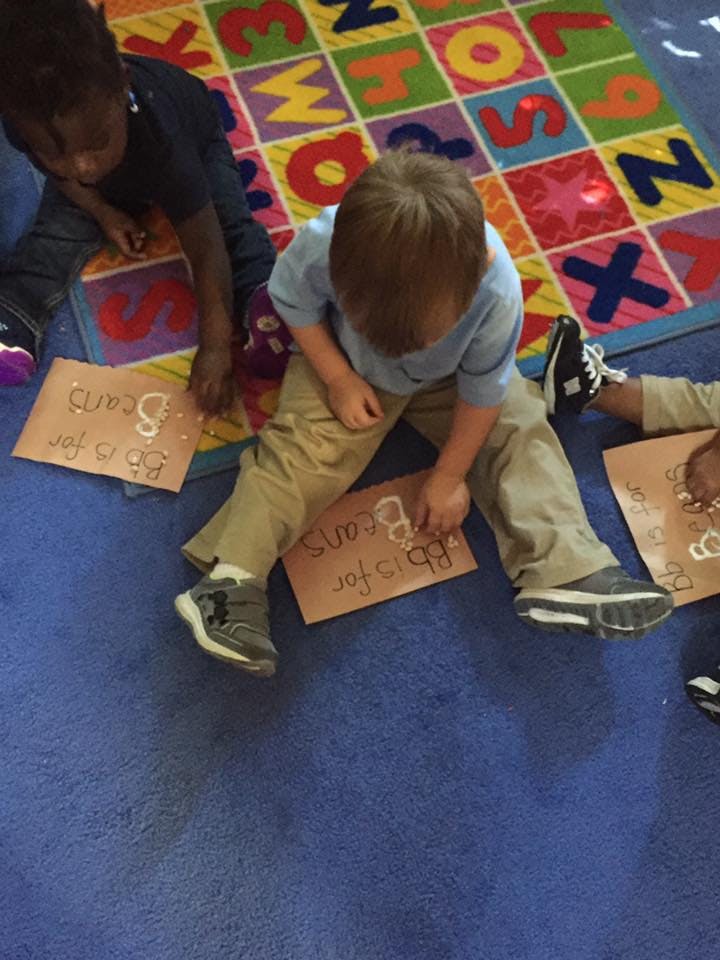 Children sitting on a colorful alphabet rug, working on craft projects