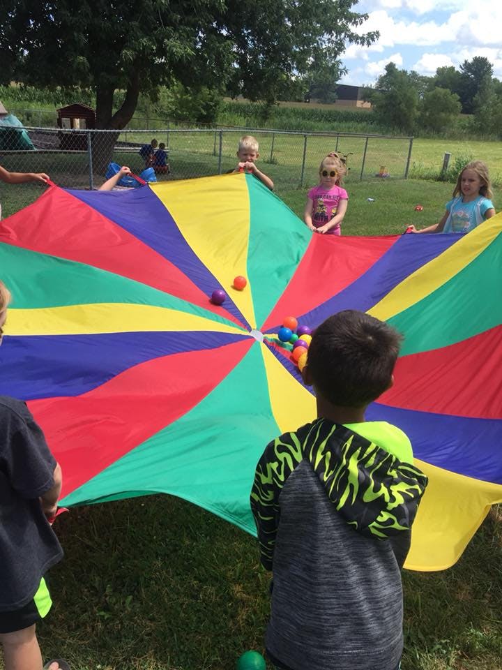 Children playing with a colorful parachute and balls outdoors