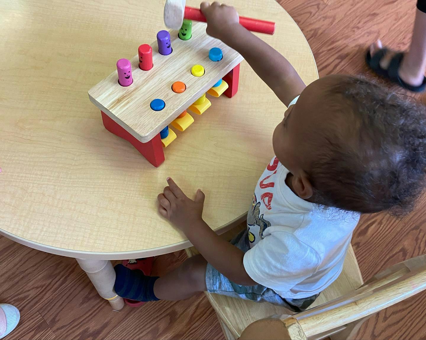 Child playing with a wooden hammer and peg toy on a table