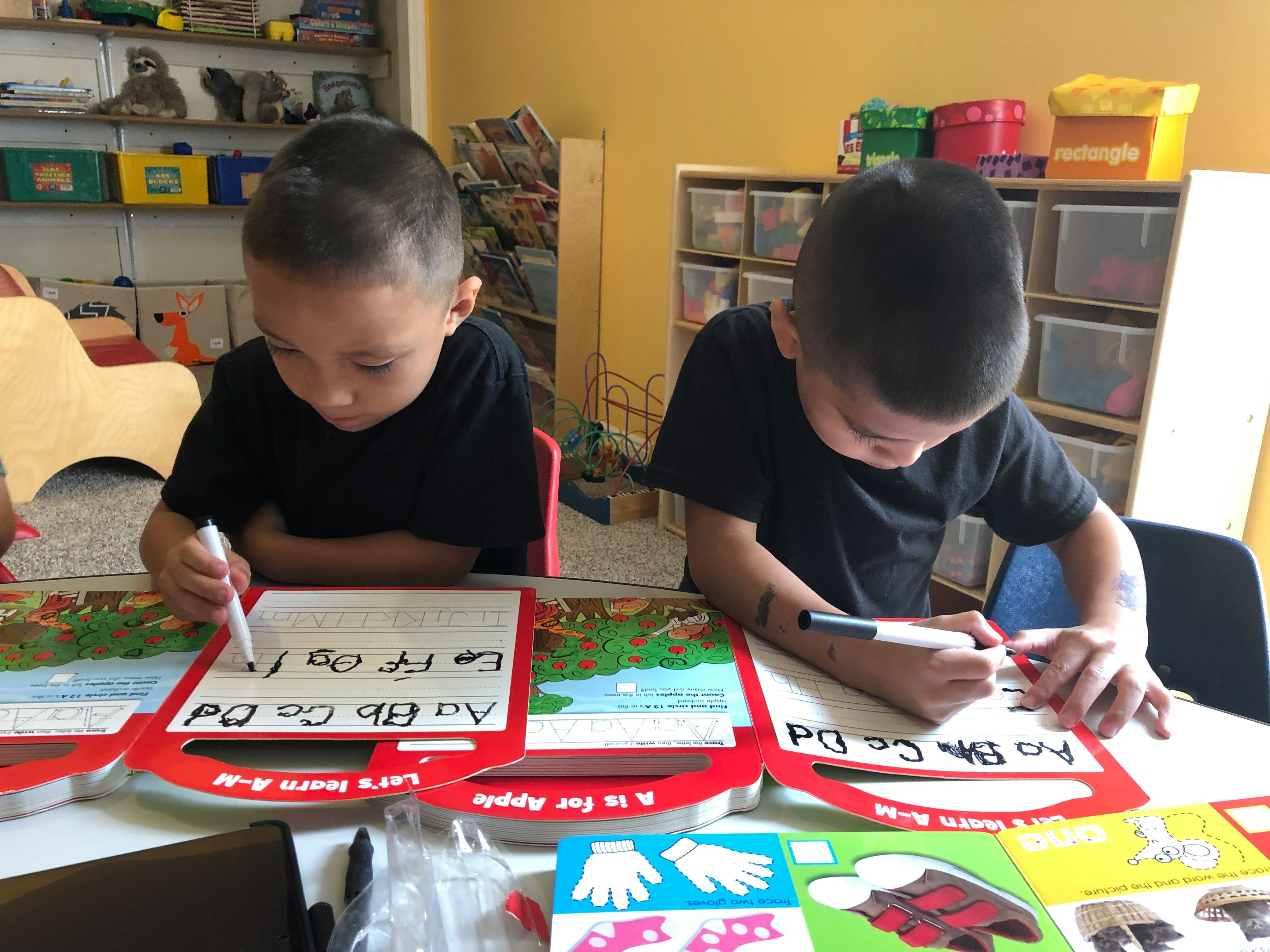Two children writing on alphabet boards in a classroom