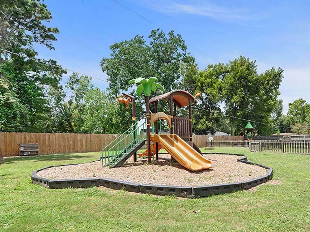 Playground with brown and orange slides, green stairs, and wood chip base