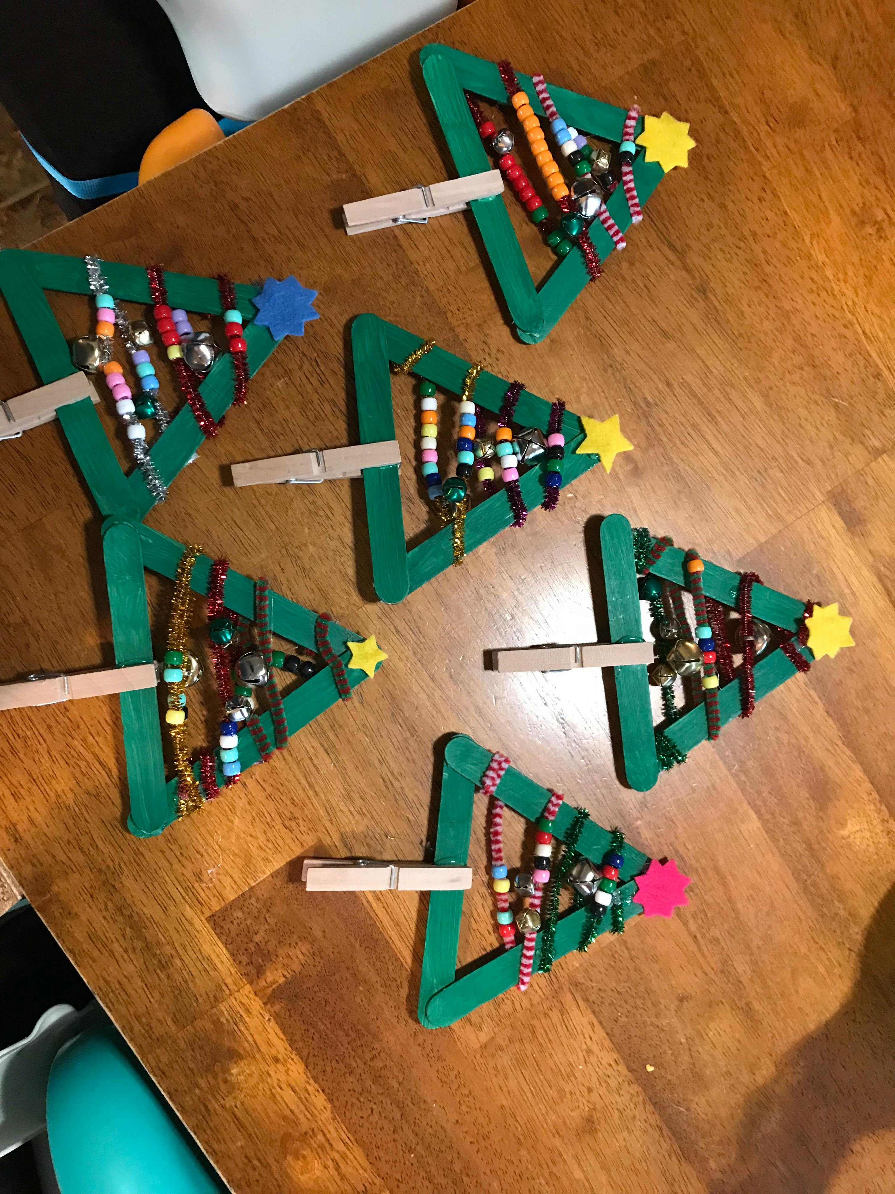 Multiple craft Christmas trees made from green popsicle sticks and beads