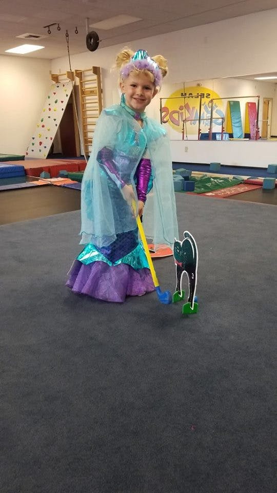 Child in costume playing mini golf with a cat-shaped obstacle