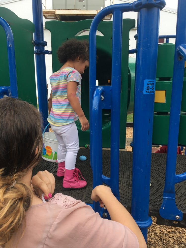 Child on a playground structure with a person in the foreground