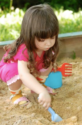 Child playing in sand with a shovel