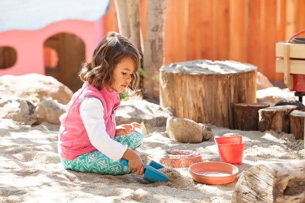 Child playing in sand with a shovel and bowls