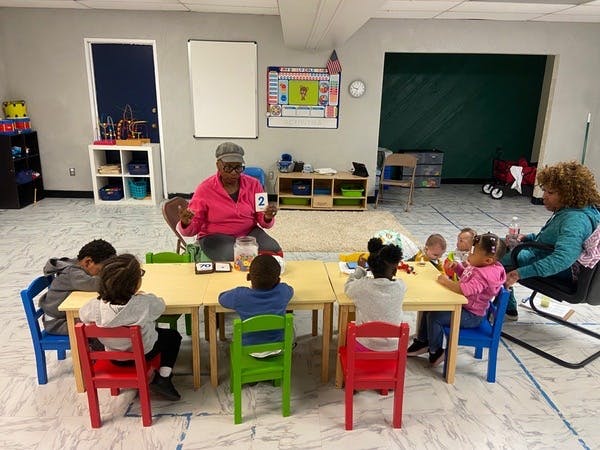 Person holding up a card with the number two to a group of children in a classroom