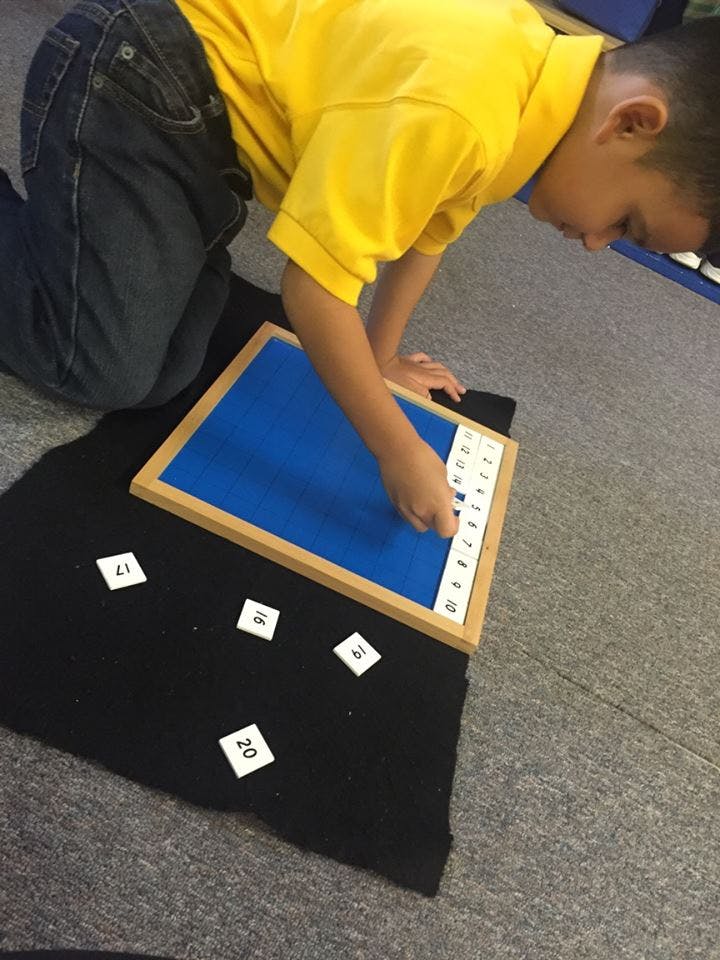 Child kneeling and placing number tiles on a board