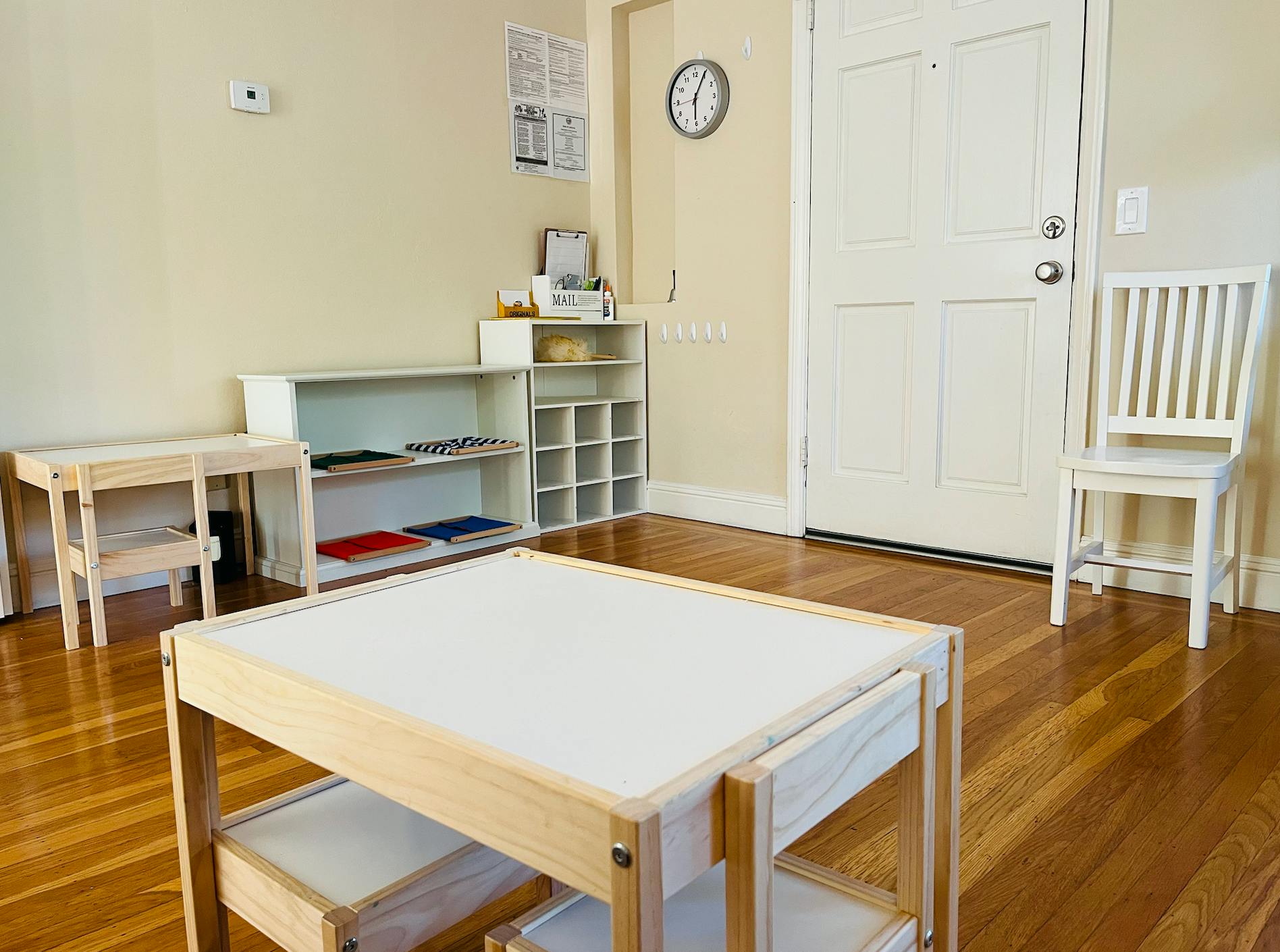 Classroom with small wooden tables and chairs, shelves with learning materials