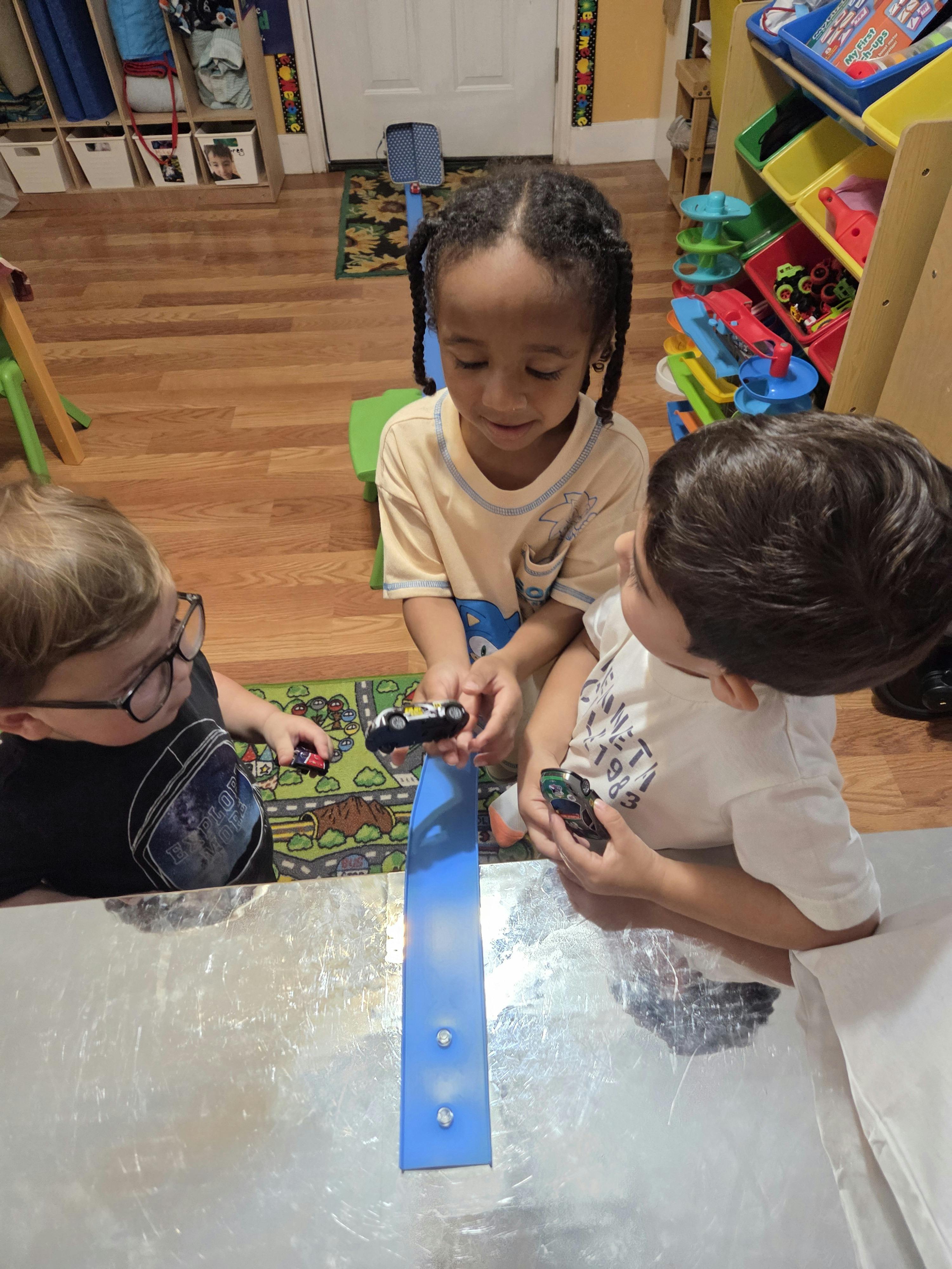 Three children playing with toy cars on a blue track