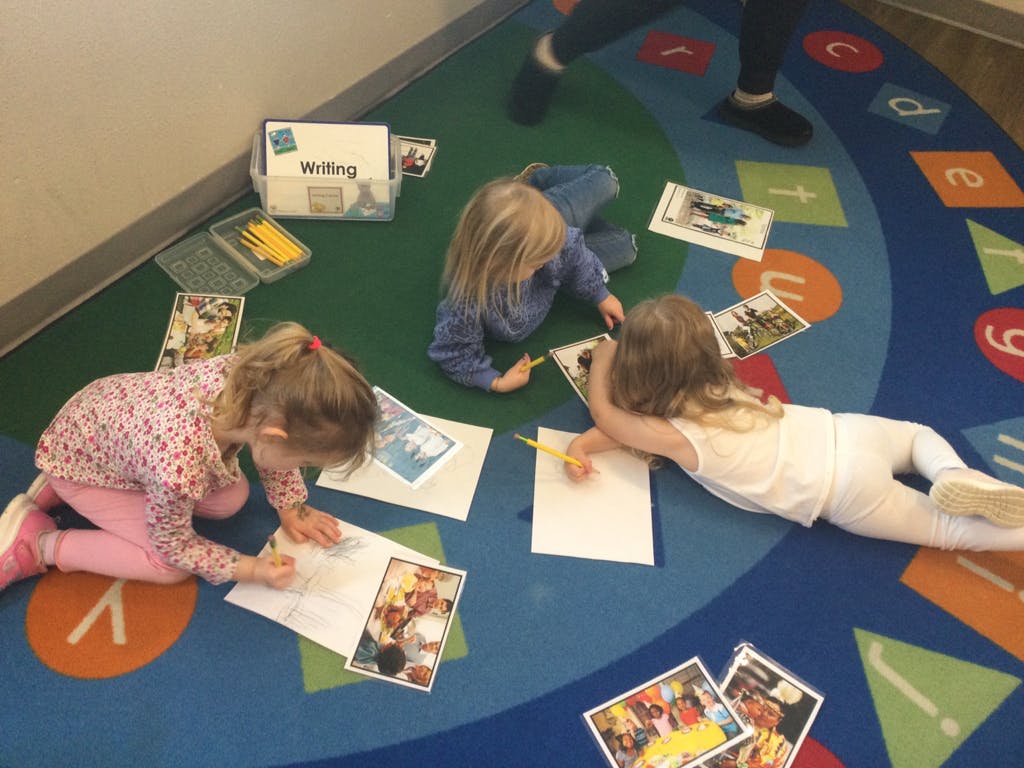 Three children drawing on paper on a colorful rug