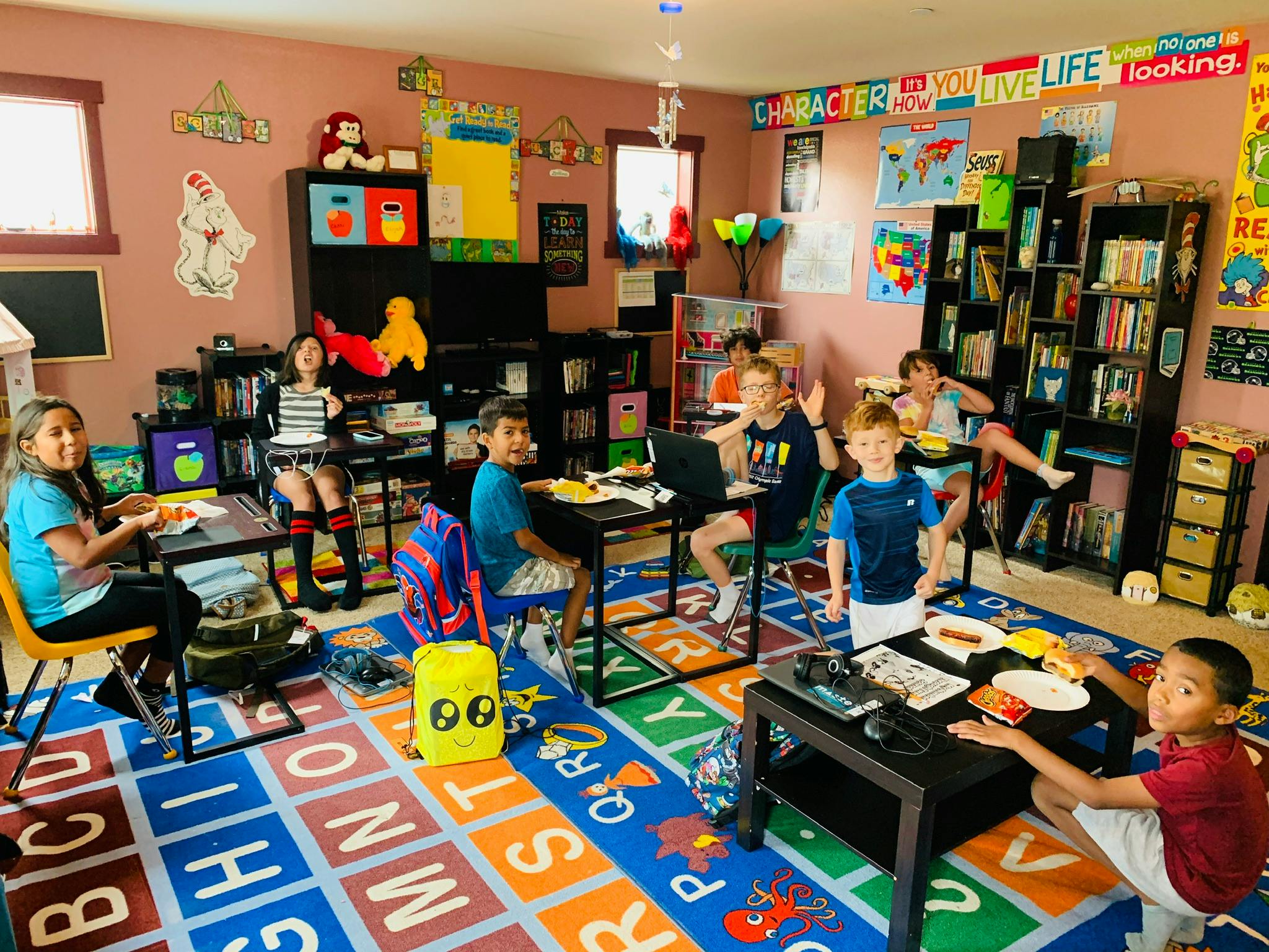 Children in a classroom sitting at desks with laptops and food